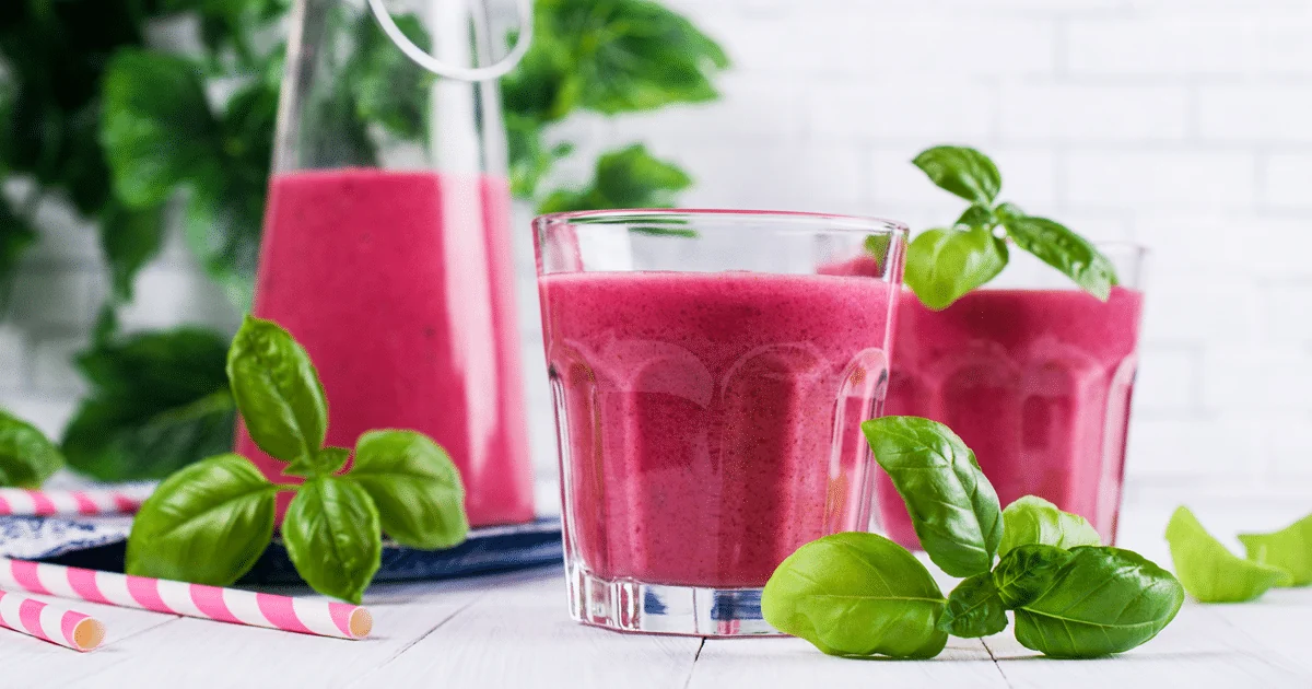 Des smoothies roses présentés avec des végétaux sur une table