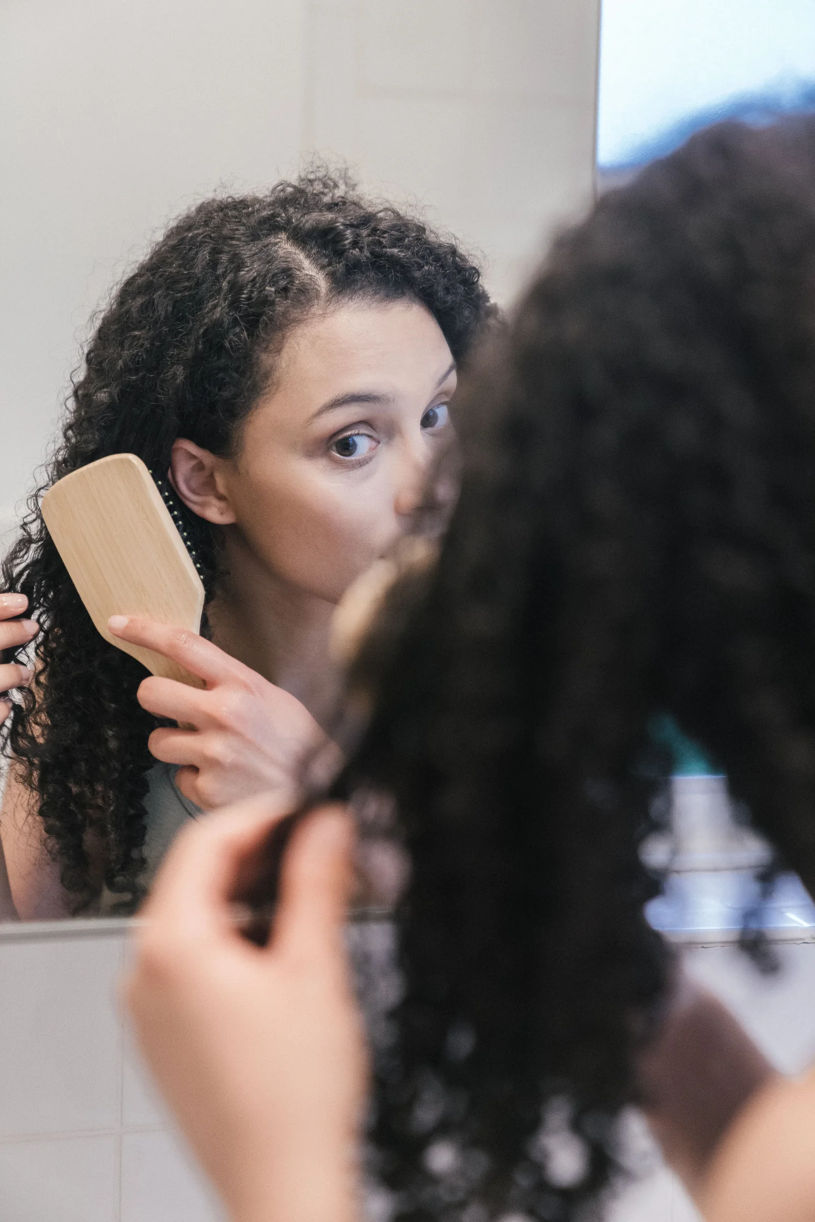 Femme aux cheveux bouclés se coiffant devant un miroir